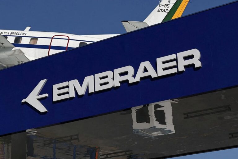 Fachada de uma loja da Embraer, fabricante brasileira de aeronaves, com destaque para o logotipo em letras brancas e fundo azul, visível no centro da imagem.