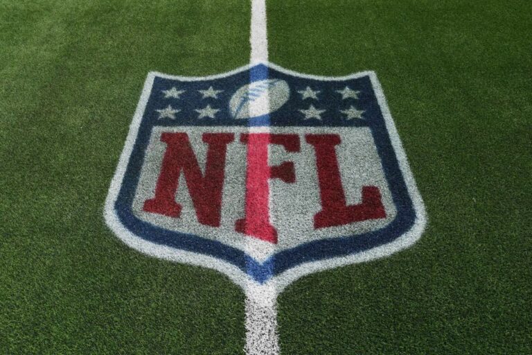 Logotipo da NFL (National Football League) pintado no centro de um campo de grama artificial verde, com as cores vermelho, branco e azul.