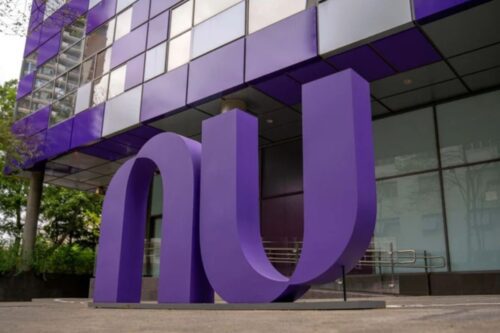 Uma escultura grande e roxa das letras 'nu', o logotipo da Nubank, em frente ao edifício de escritórios da empresa, que também tem detalhes em roxo e espelhado.