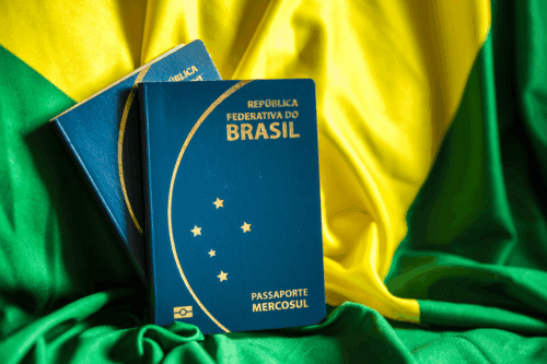 Passaporte da República Federativa do Brasil em destaque sobre uma bandeira do Brasil, com cores verde, amarelo e azul ao fundo.