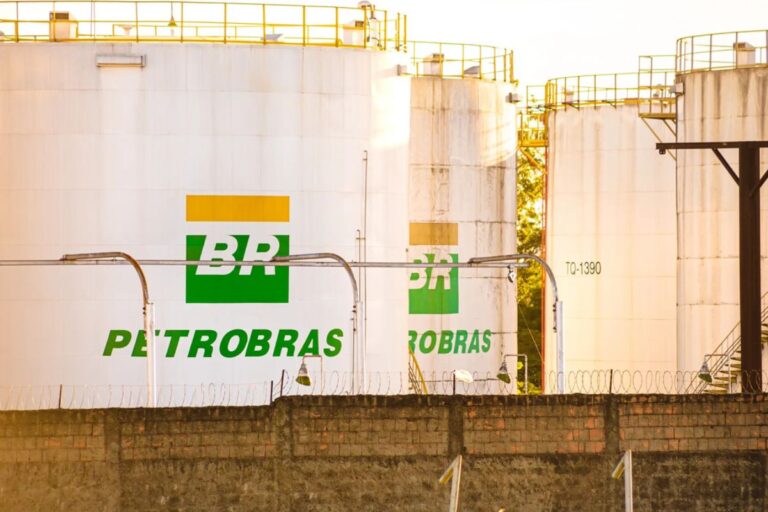 Grandes tanques de armazenamento de combustível, brancos e cilíndricos, com o logotipo da Petrobras (BR verde e amarelo) pintado em suas laterais.