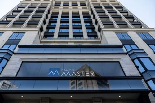 Fachada em ângulo baixo de um prédio alto e moderno, com a logomarca e o nome 'BANCO MASTER' visíveis em letras brancas e azuis no vidro sobre a entrada.