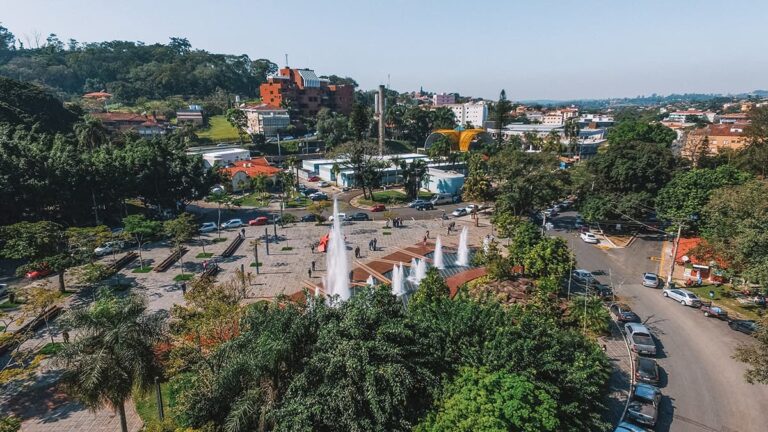 Vista aérea da Praça Dr. Octávio Moura Andrade em Águas de São Pedro, com fontes, área verde e prédios ao redor.