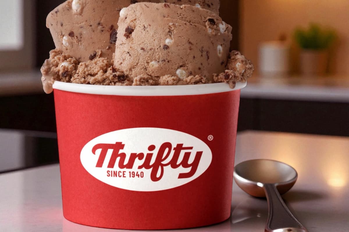 Sorvete Thrifty Ice Cream em pote vermelho com logo da marca e colher ao lado em ambiente iluminado.