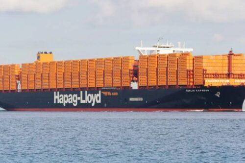 Navio porta-contêineres da Hapag-Lloyd carregado de contêineres laranja navegando no mar, símbolo da expansão da gigante alemã no setor portuário.