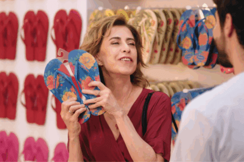 Cena de campanha publicitária da Havaianas com a atriz Fernanda Torres escolhendo modelos de chinelos estampados em uma loja oficial