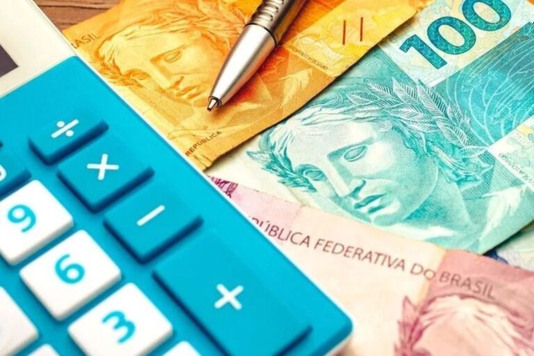 calculadora azul, caneta e notas de dinheiro brasileiro (reais) em diferentes cores (R$ 100, R$ 50 e R$ 20) sobre uma mesa.