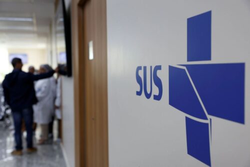 Uma visão em close-up e ângulo lateral do logotipo do SUS (Sistema Único de Saúde) na parede de uma unidade de saúde.